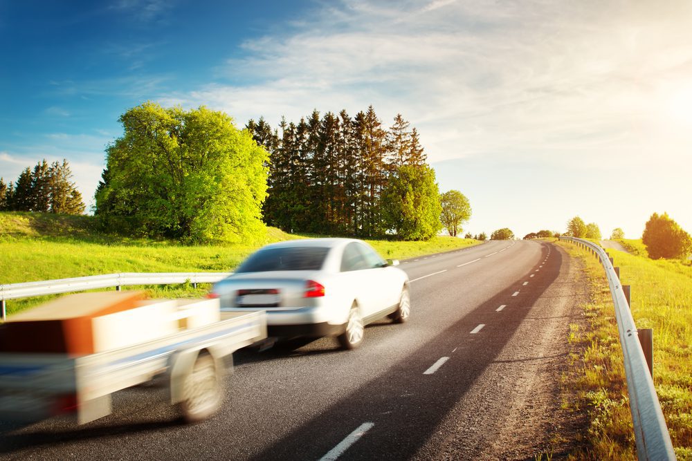 Asphalt,Road,On,Dandelion,Field,With,A,Car,With,Trailer. Auto mit Anhänger - Haftung bei verlorenen Teilen die eine Unfall verursachen