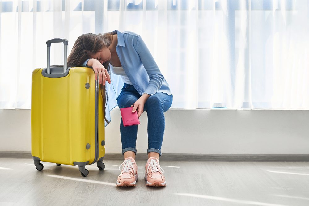 Woman,Traveler,With,Yellow,Suitcase,Affected,By,Flight,Delay,And Nutzlos aufgewendete Urlaubszeit