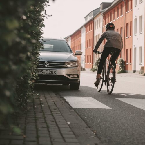 Fahrzeug verlässt Einfahrt und kollidiert mit einem Radfahrer, der die Radspur verlässt.